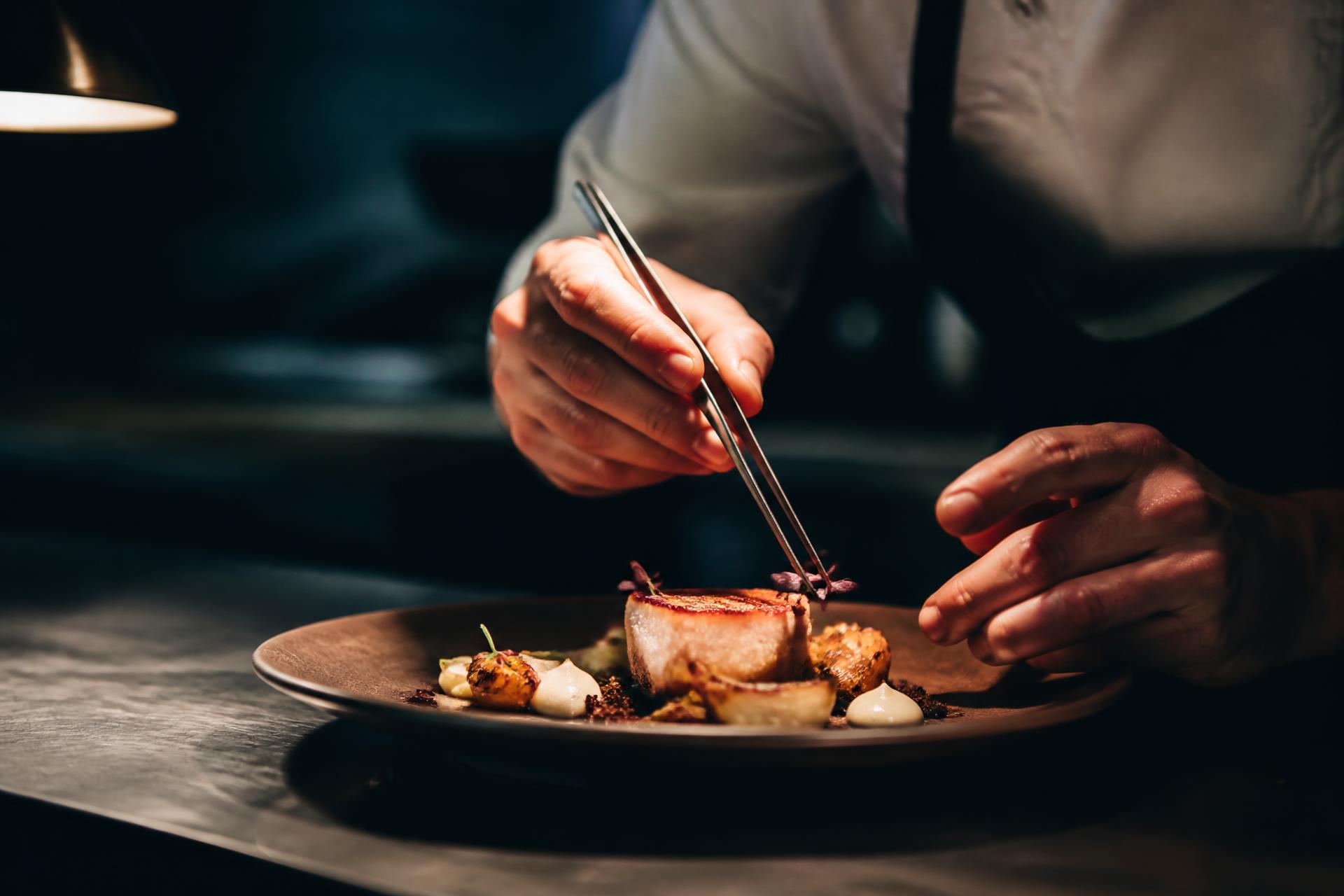 Chef Isaac Behr plating a fine-dining course with tweezers